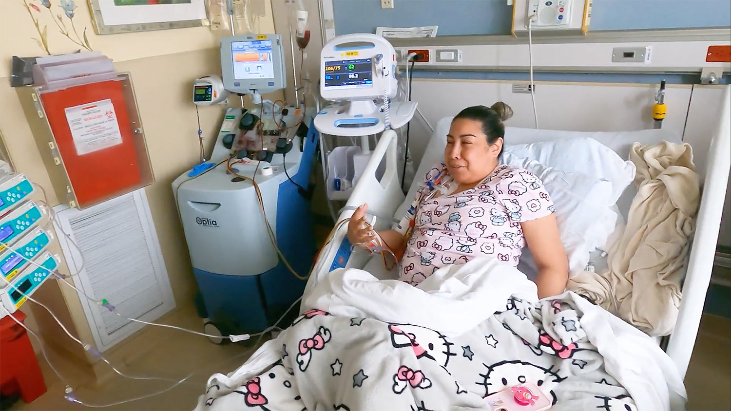 Jessica Ceja sits in a hospital bed in hello kitty pajamas hooked up to an infusion machine